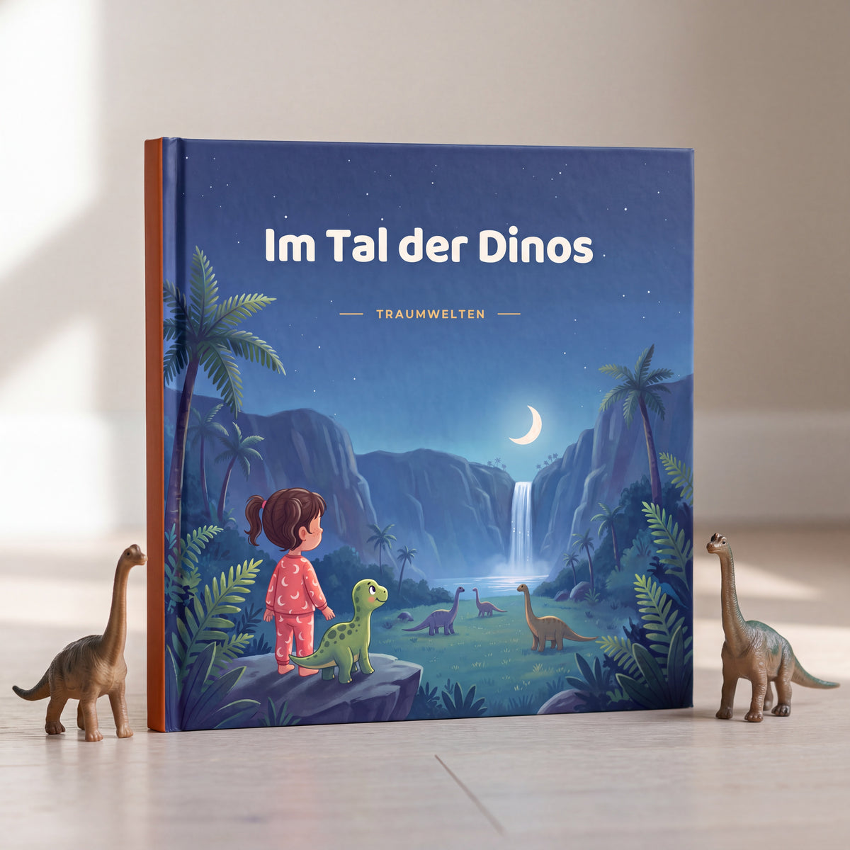 Hardcover Im Tal der Dinos stehend zwischen zwei Spielzeugdinos, orangener Buchruecken sichtbar